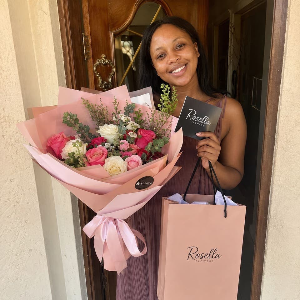 A customer holding a pink Rosella bouquet and branded gift bag at her front door