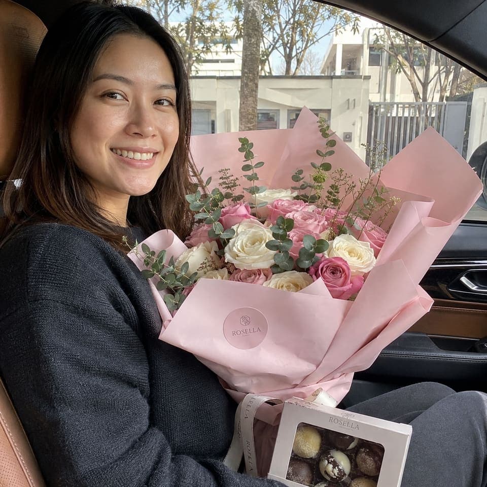 A customer smiling with a pink Rosella bouquet and chocolates in her car