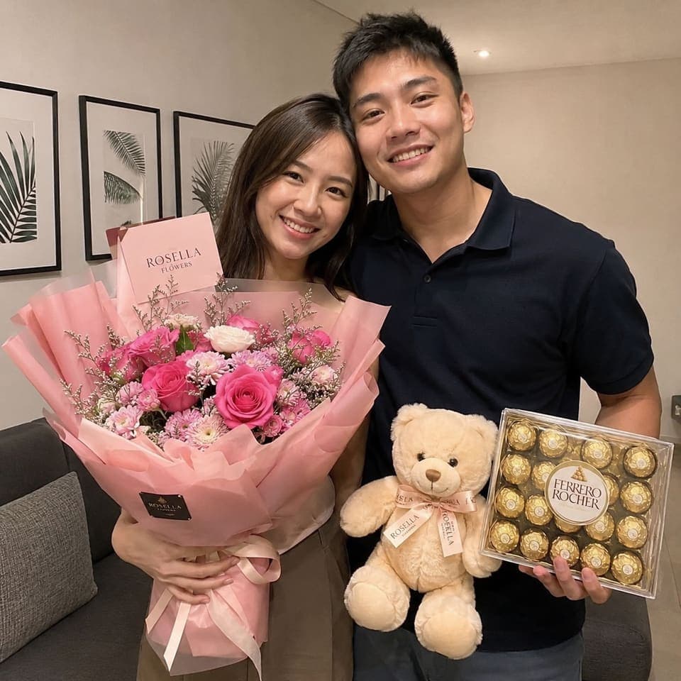 A couple holding a Rosella bouquet, teddy bear and box of chocolates