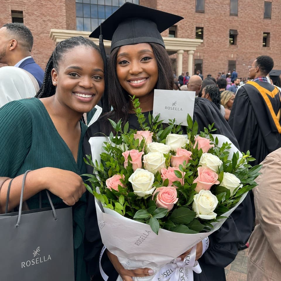 Two women celebrating graduation with a pink and white bouquet