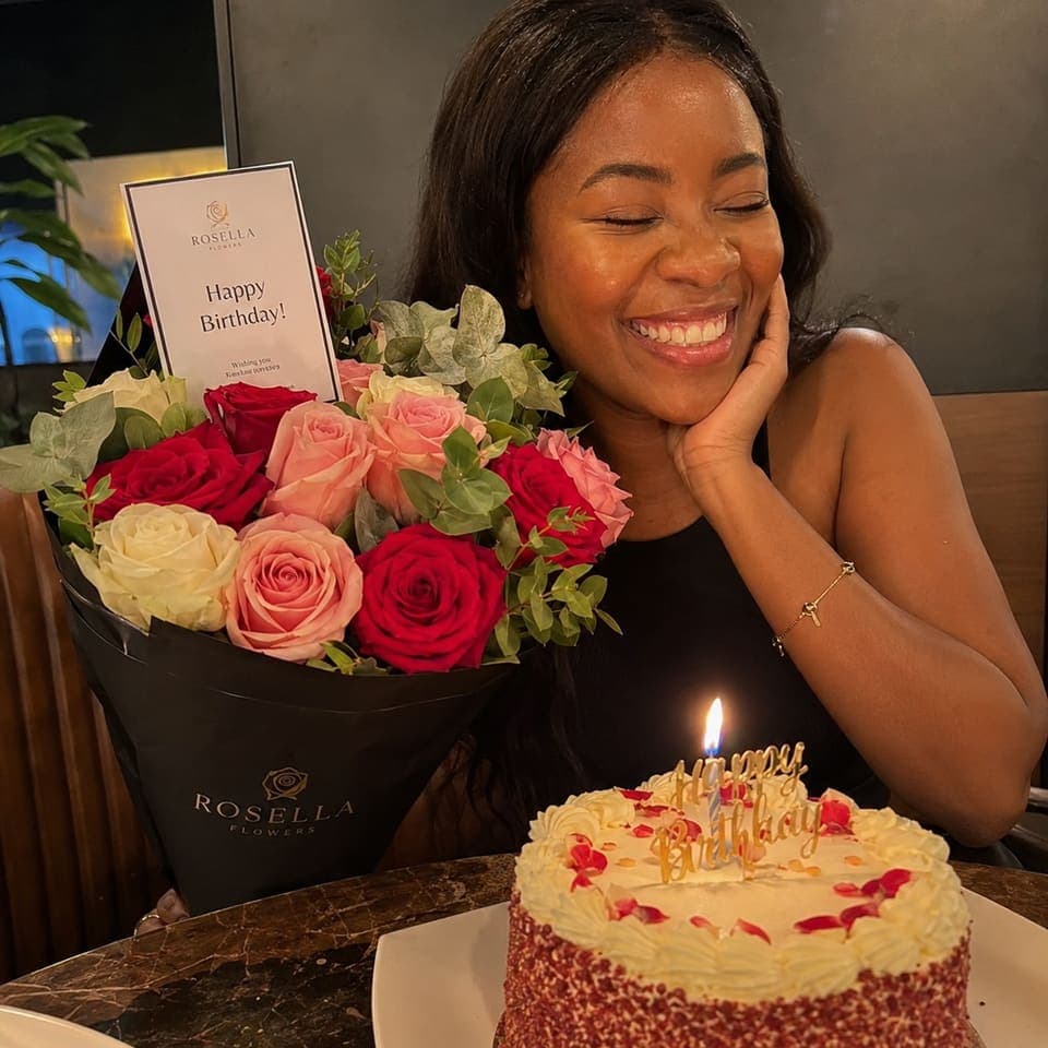 A birthday customer smiling beside a rose arrangement and celebration cake