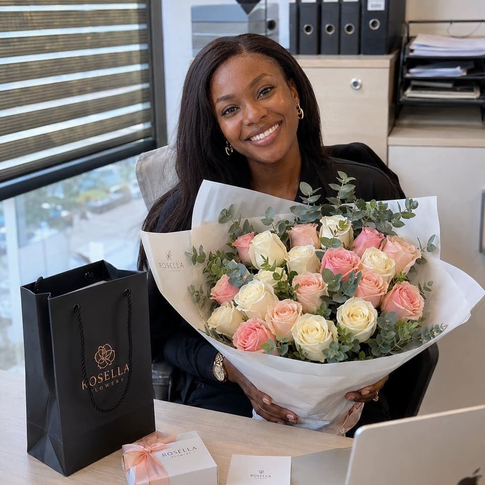 A professional smiling at her desk with a pale pink rose bouquet