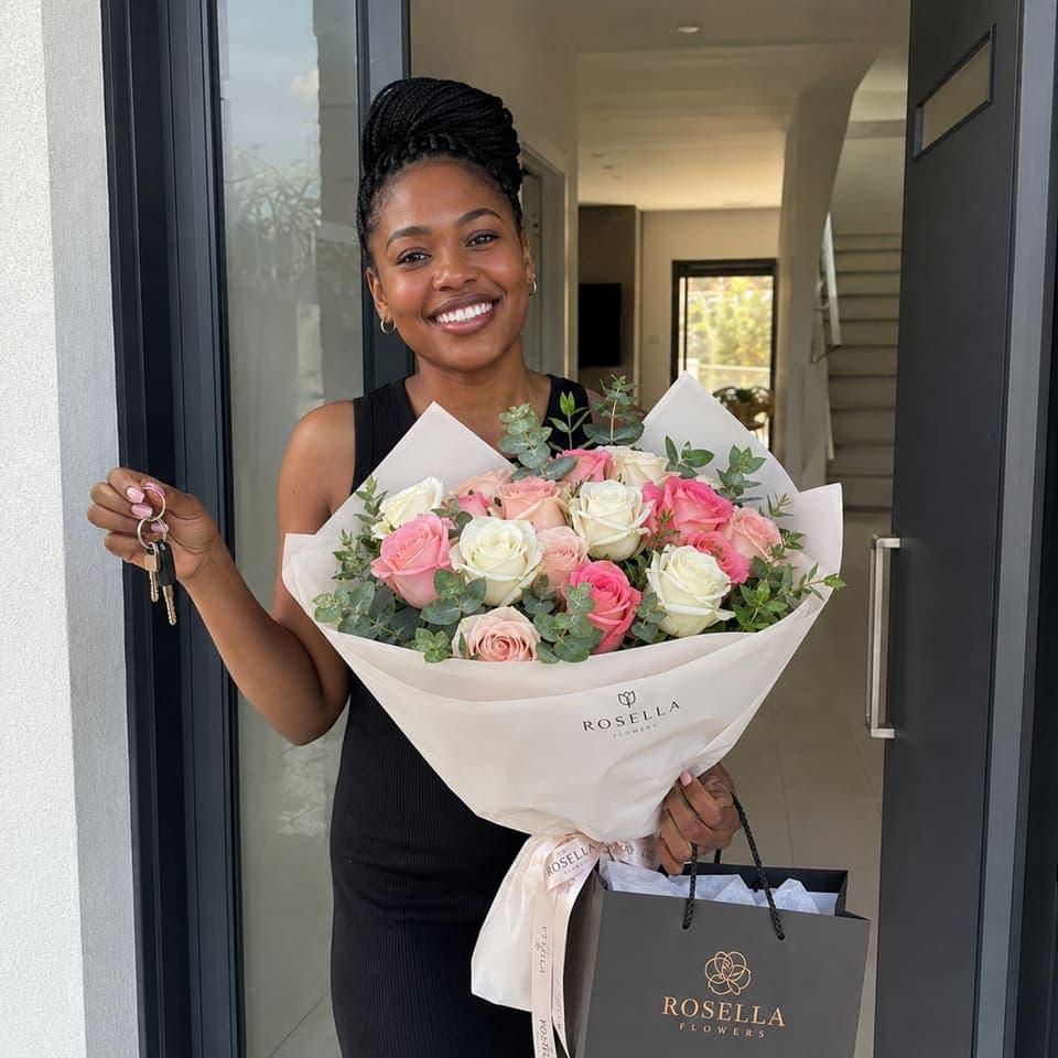 A customer holding new keys, a Rosella bouquet and branded gift bag