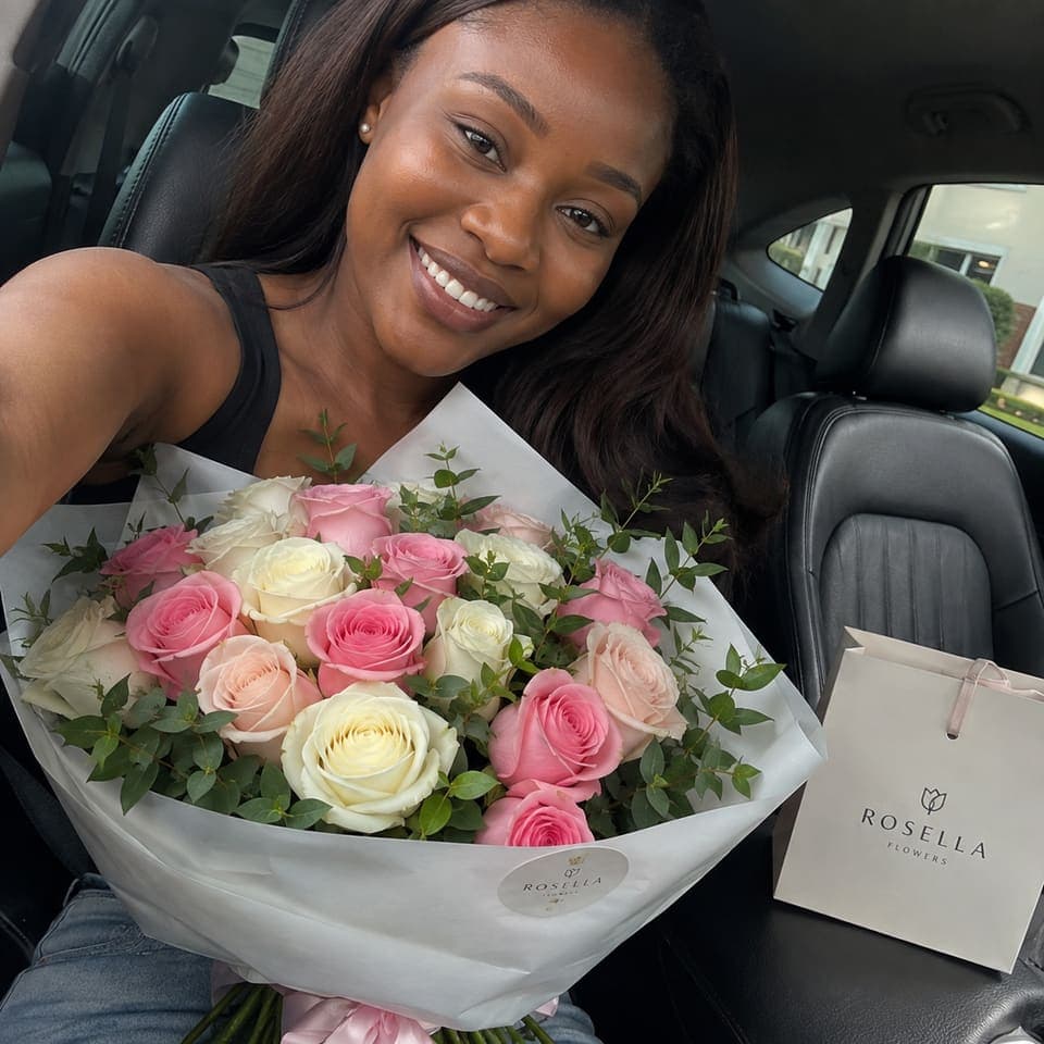 A customer smiling in her car with a pink and white rose bouquet