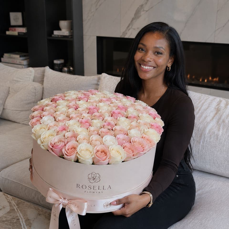 A customer holding a large round arrangement of pale pink roses at home